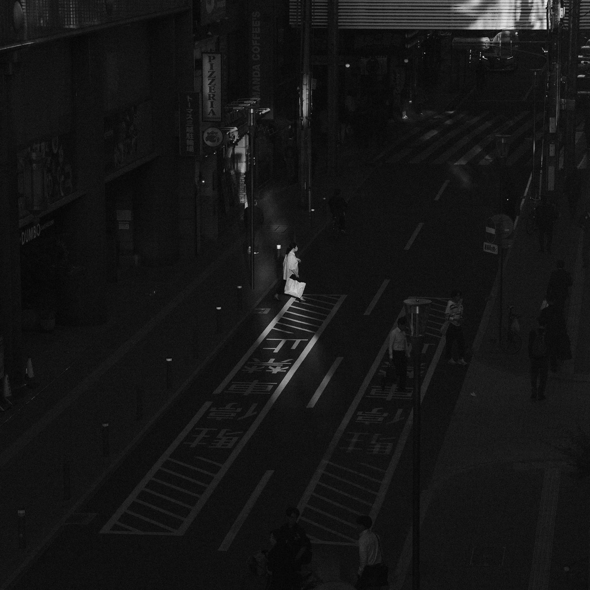 An overhead view of pedestrians crossing a dark city street at night.