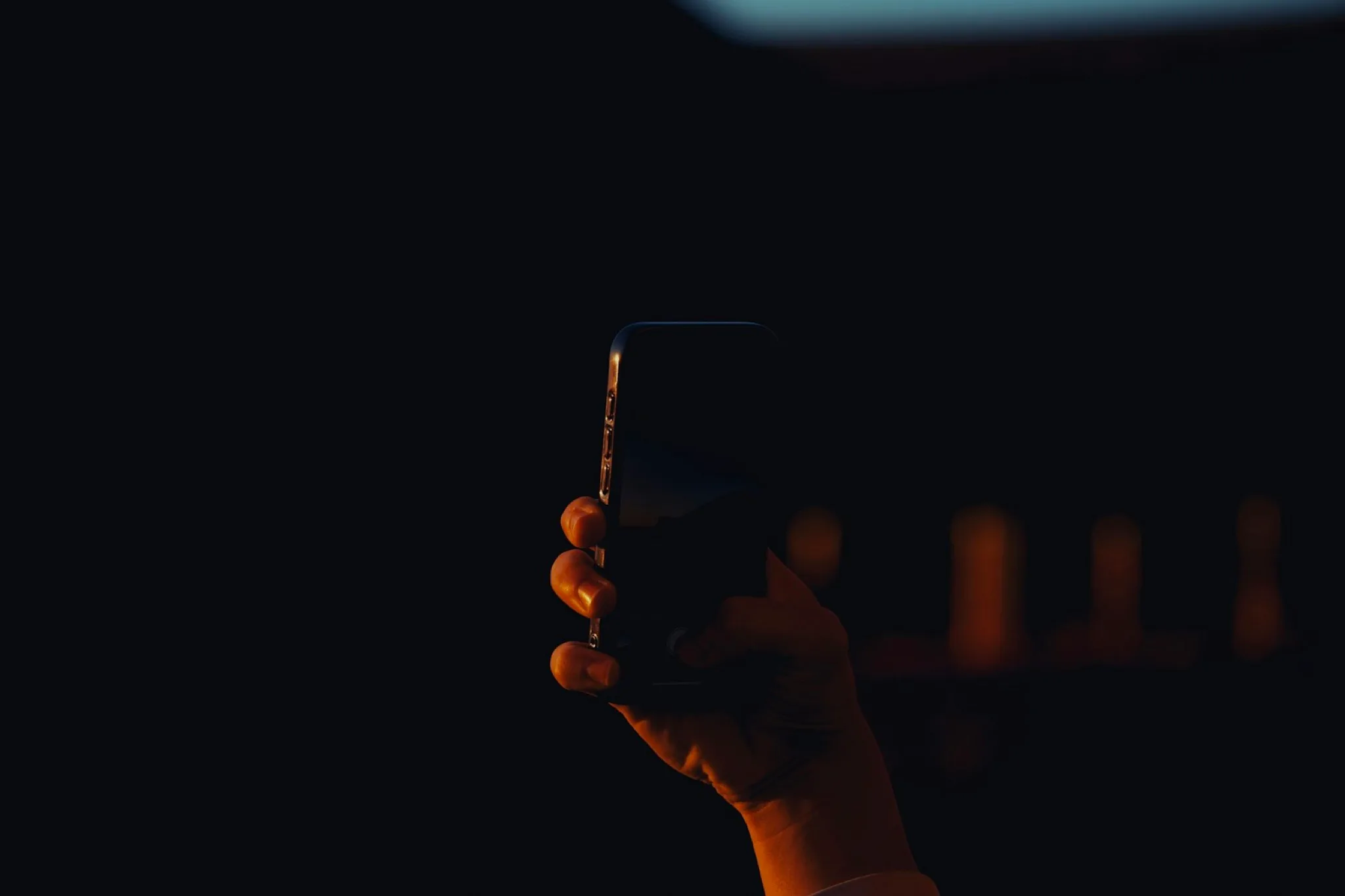 A hand holding a smartphone against a dark background.